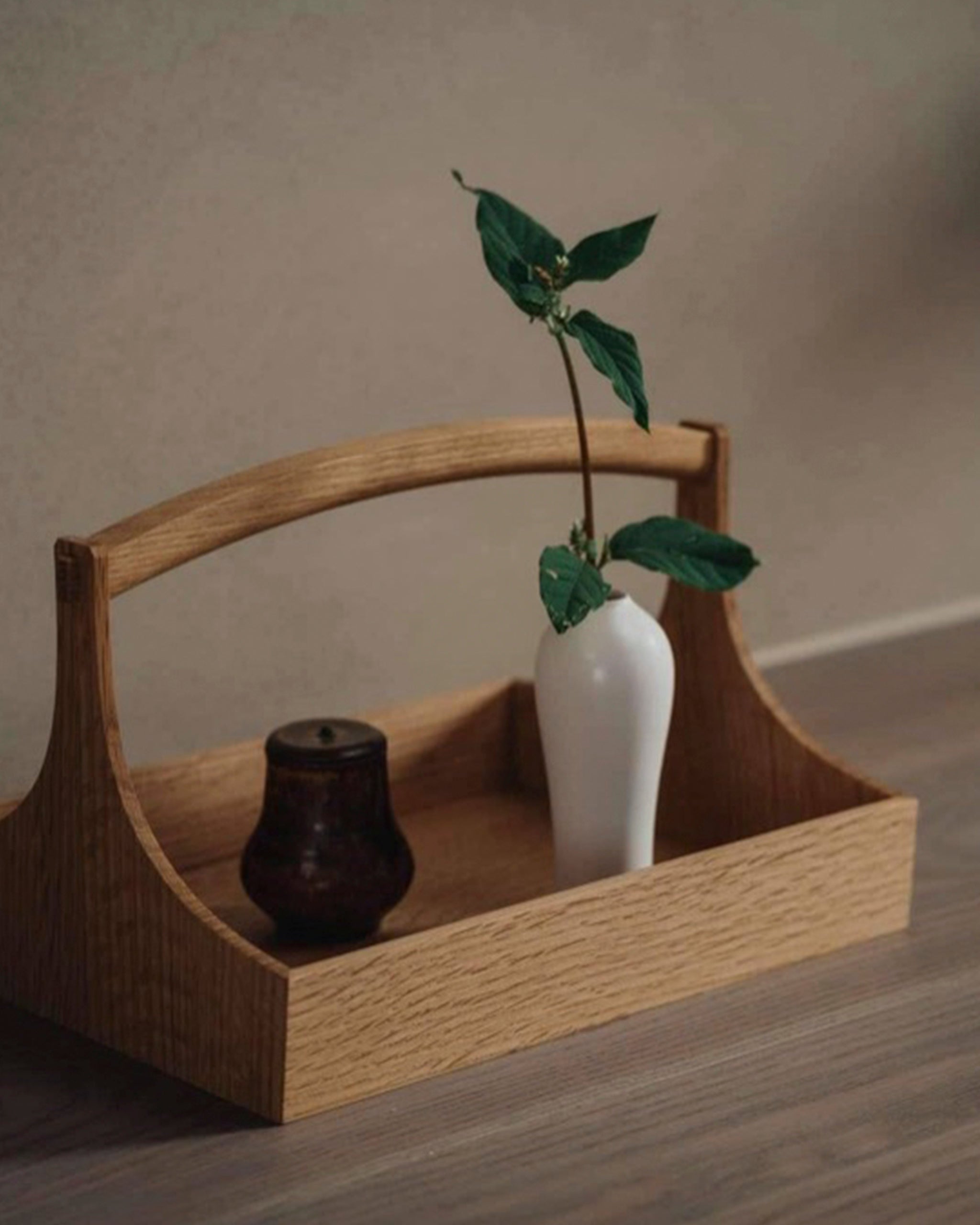 Large wooden table caddy by Aizawa with short handles, carrying a white vase with leaves and a jar on a wooden surface