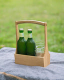 Wooden table caddy by Aizawa with two green bottles and two glass cups stacked on blanket with a grass background.