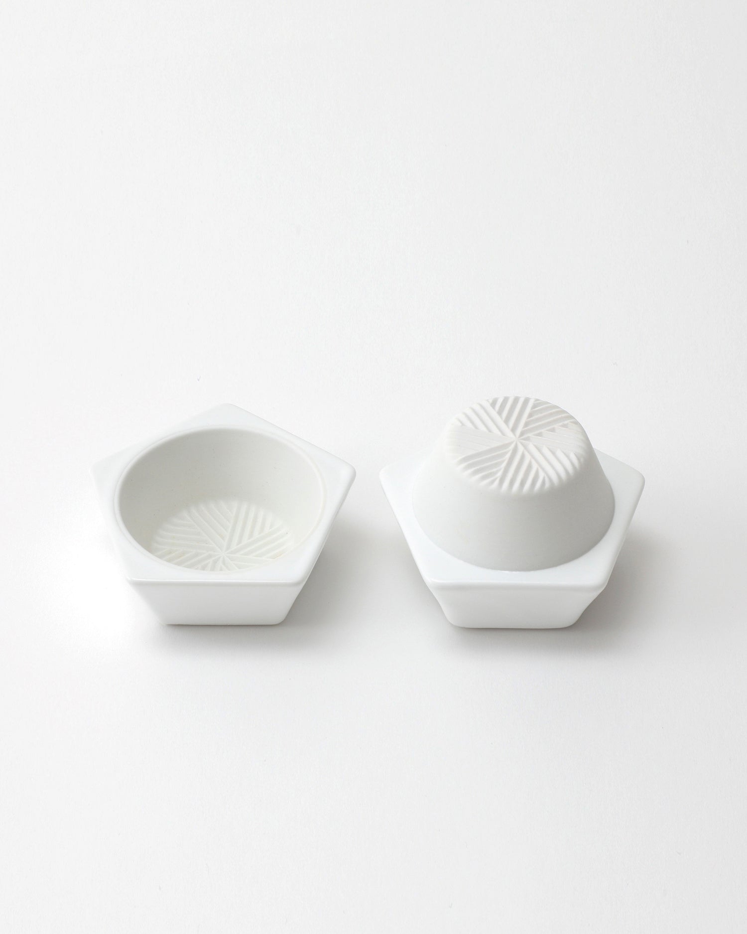 Opened white geometric spice mill with a grated interior design on a light gray background