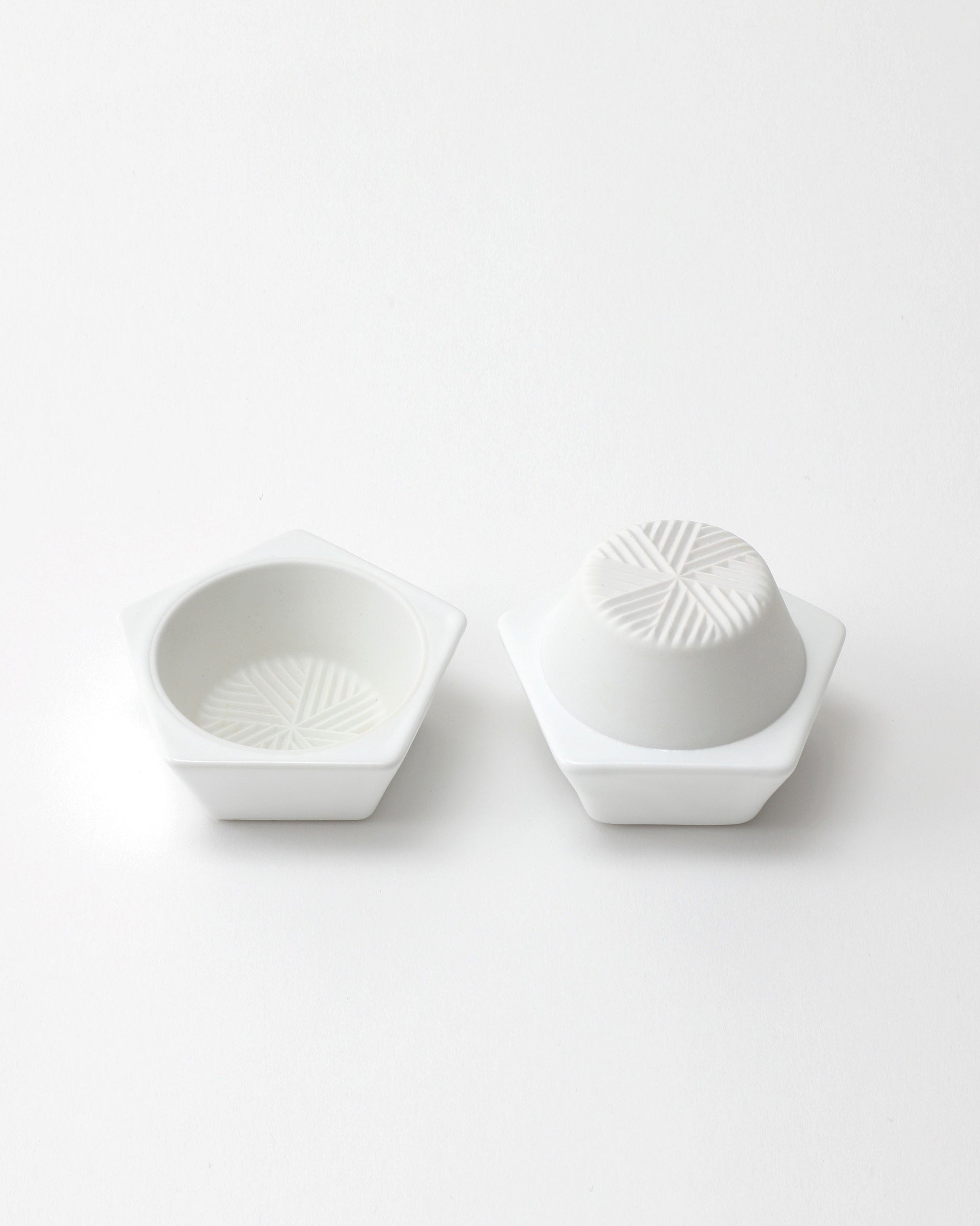 Opened white geometric spice mill with a grated interior design on a light gray background