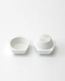 Opened white geometric spice mill with a grated interior design on a light gray background