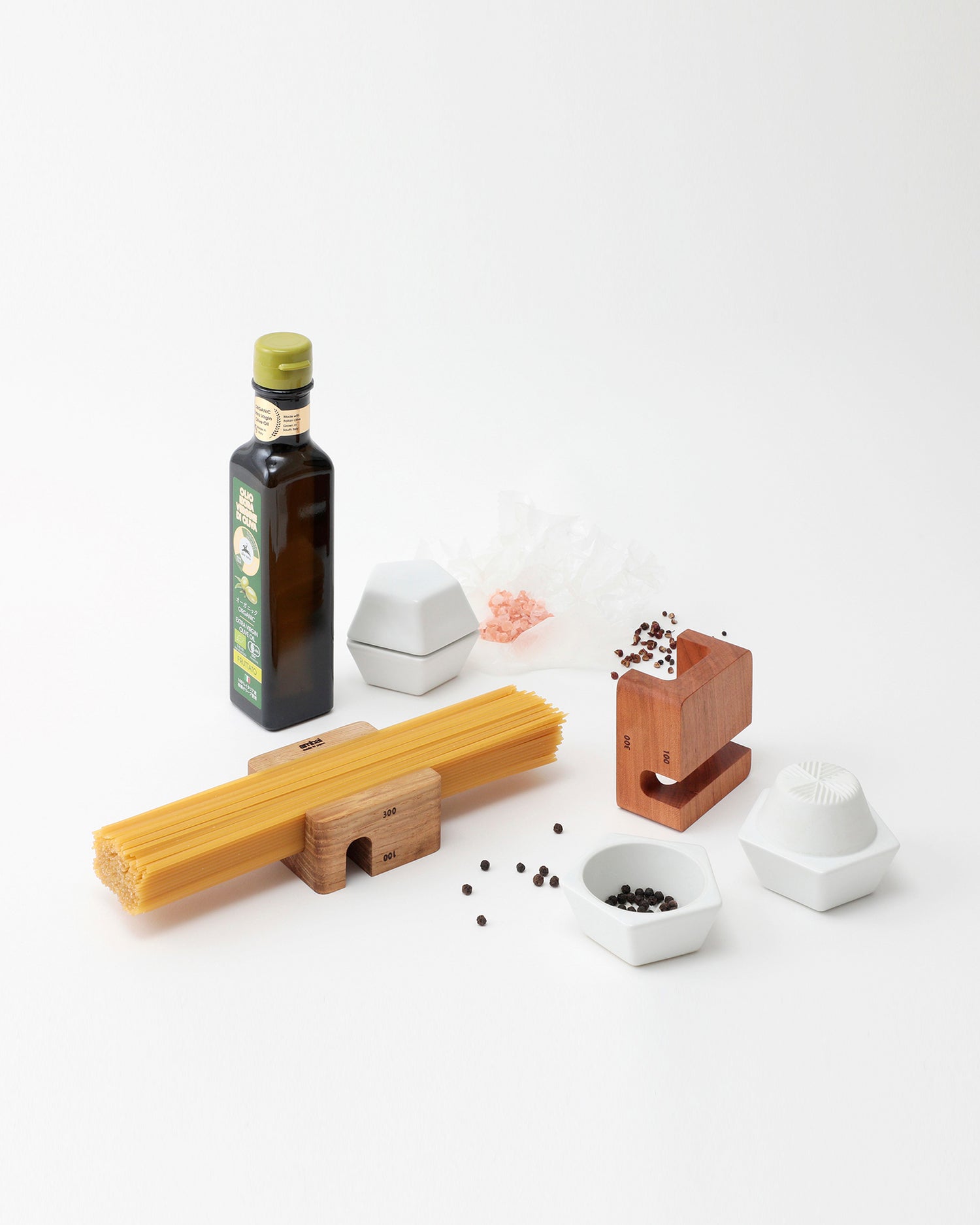 Collection of kitchen items including an oil bottle, wooden holders, and spice mill containers with black pepper on a white background