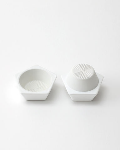 Opened white geometric spice mill with a grated interior design on a light gray background