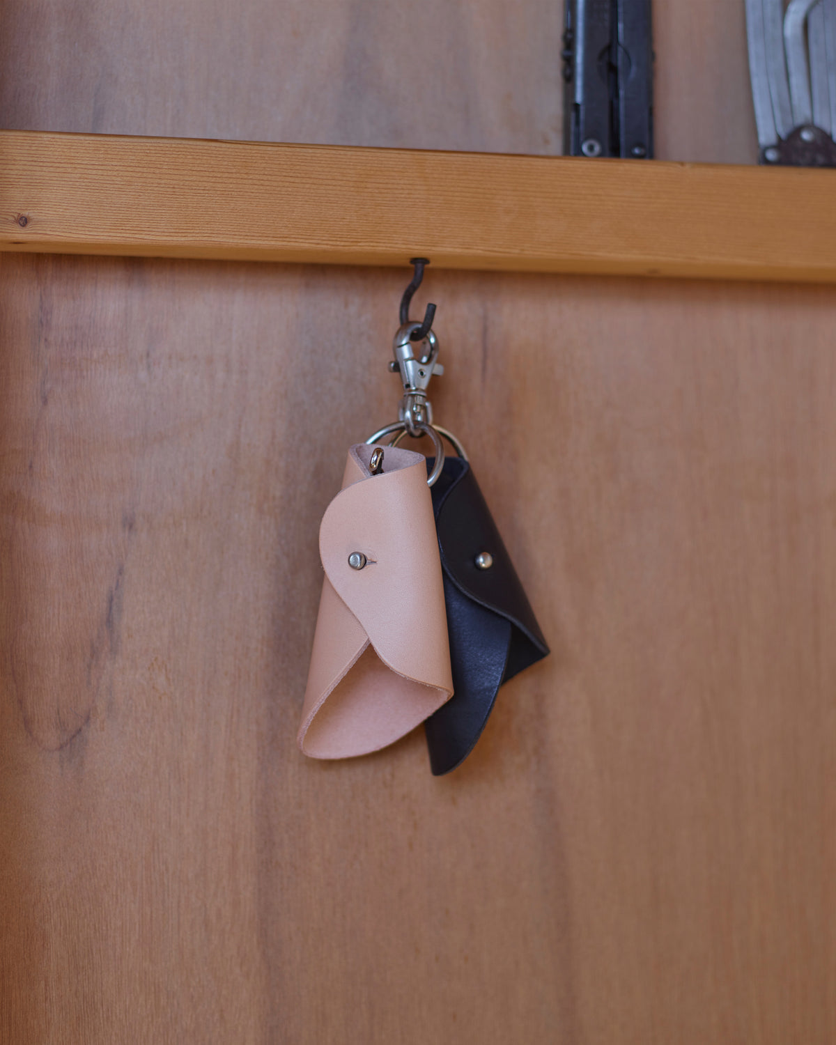 Two small Circle Cut Out Key Chains in nataural and black by Hender Scheme and Artek hanging on a hook with a wooden backdrop