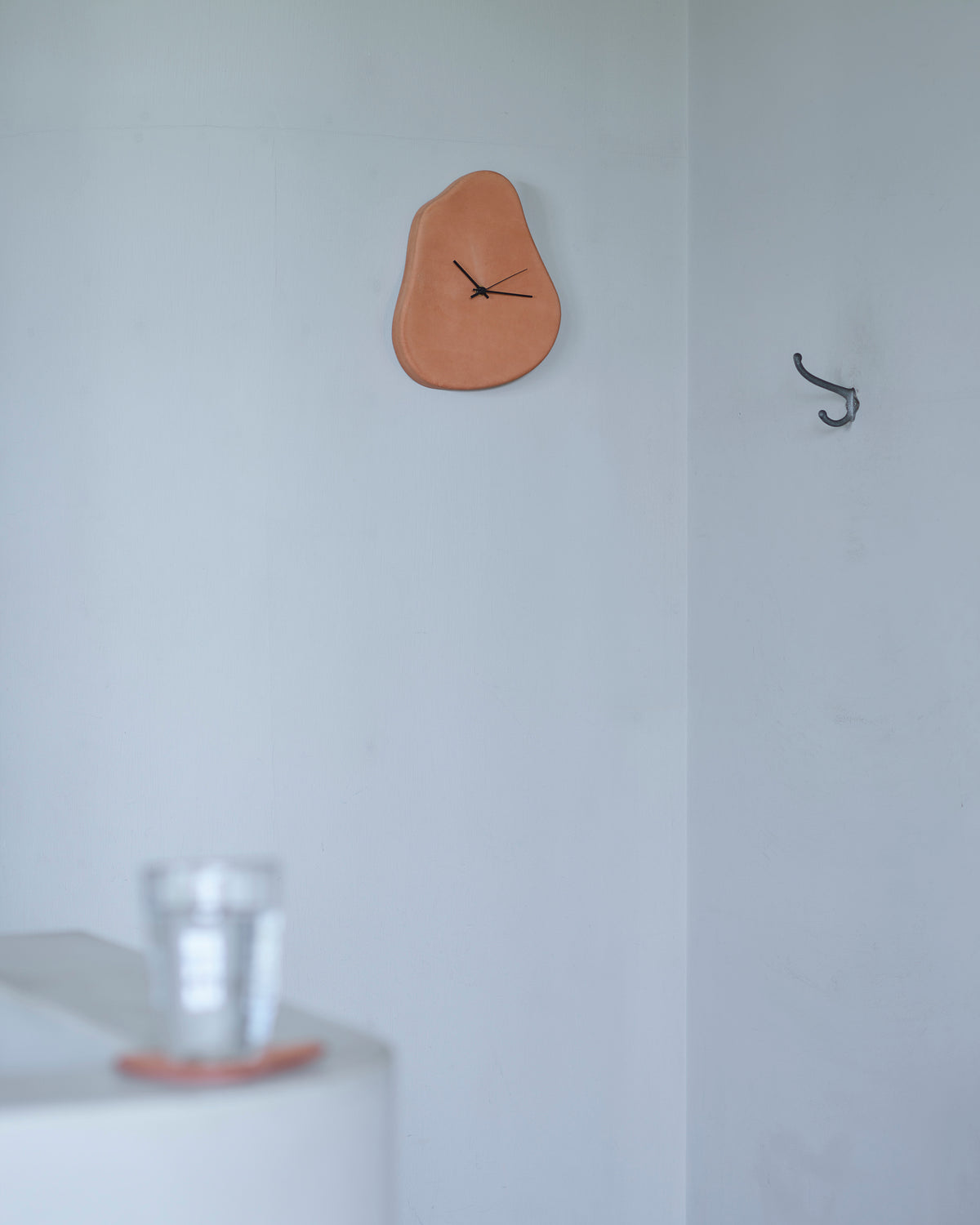 Leather Clock by Hender Scheme hanging on a white wall with a cup and coaster in the forefront 