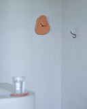 Leather Clock by Hender Scheme hanging on a white wall with a cup and coaster in the forefront 