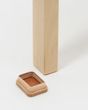 Up-close of stool foot next to leather shoe by Artek and Hender Scheme on a  gray background
