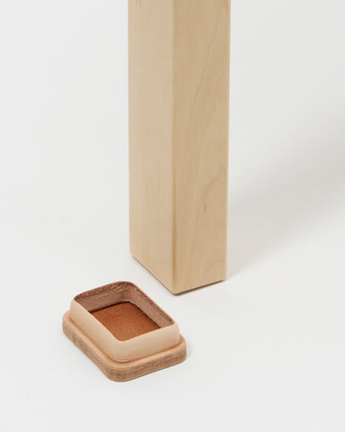 Up-close of stool foot next to leather shoe by Artek and Hender Scheme on a  gray background