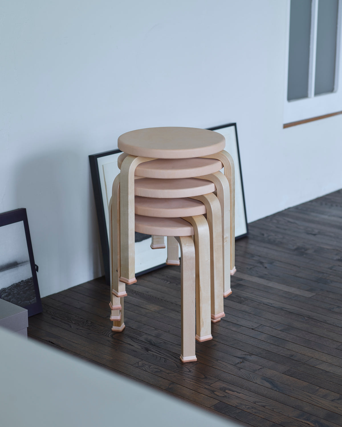Five stools stacked wearing shoes by Artek and Hender Scheme on a wooden floor and white wall