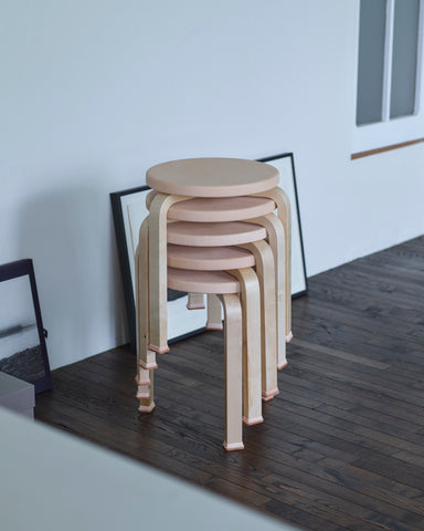 Five stools stacked wearing shoes by Artek and Hender Scheme on a wooden floor and white wall