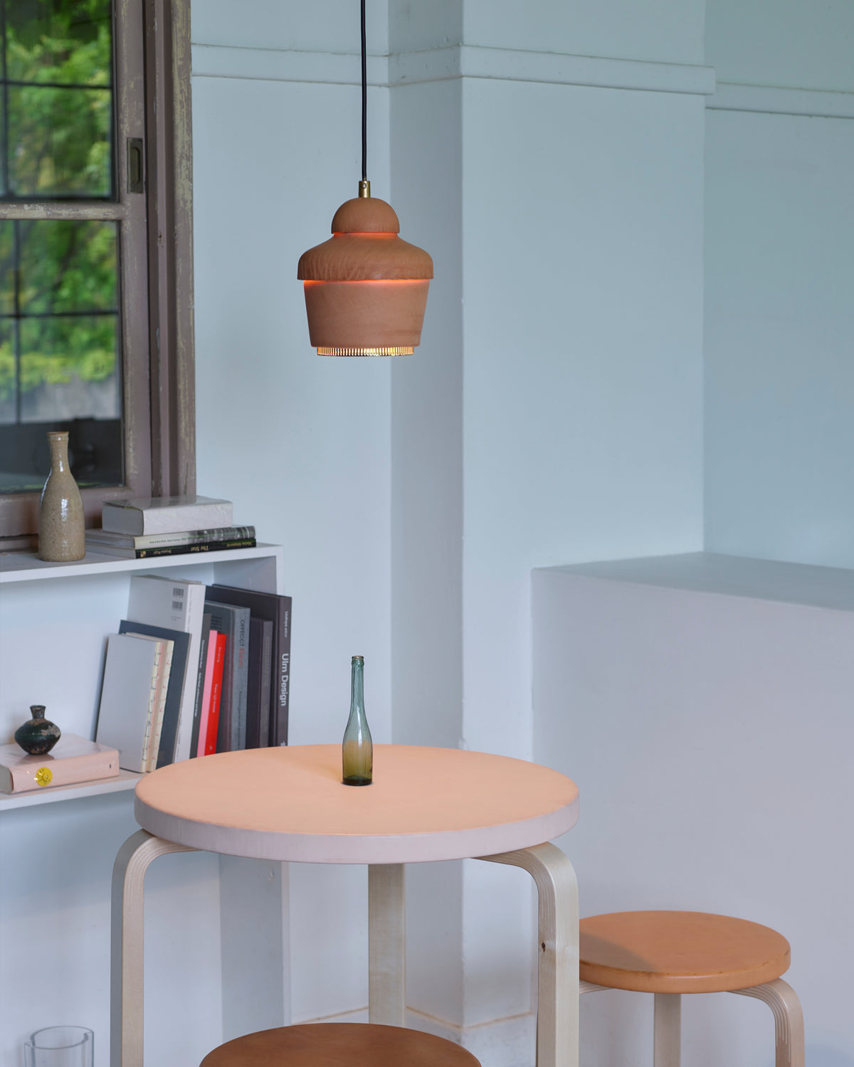 Leather table, stools, pendant light by Hender Scheme and Artek in a room with a bookshelf in the background