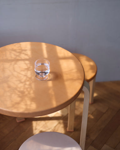 Leather table with shoes and stools by Hender Scheme and Artek with a glass of water sitting on the table in a room