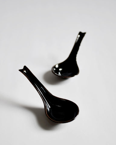 Front view of 2 staggered black Ceramic Soup Spoons by Azmaya against white-gray background. 