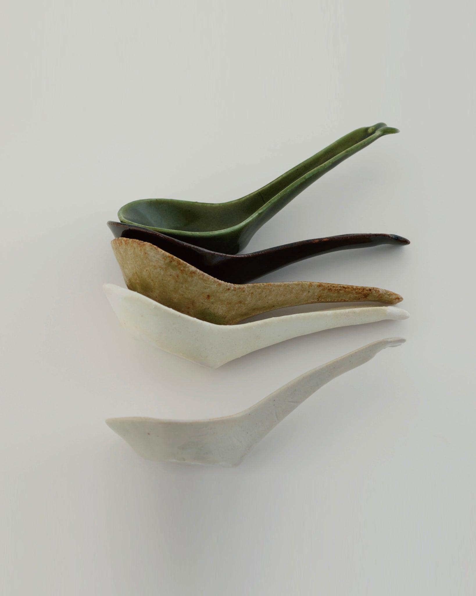 Side view of 5 Ceramic Soup Spoons in varying colors by Azmaya against white-gray background.