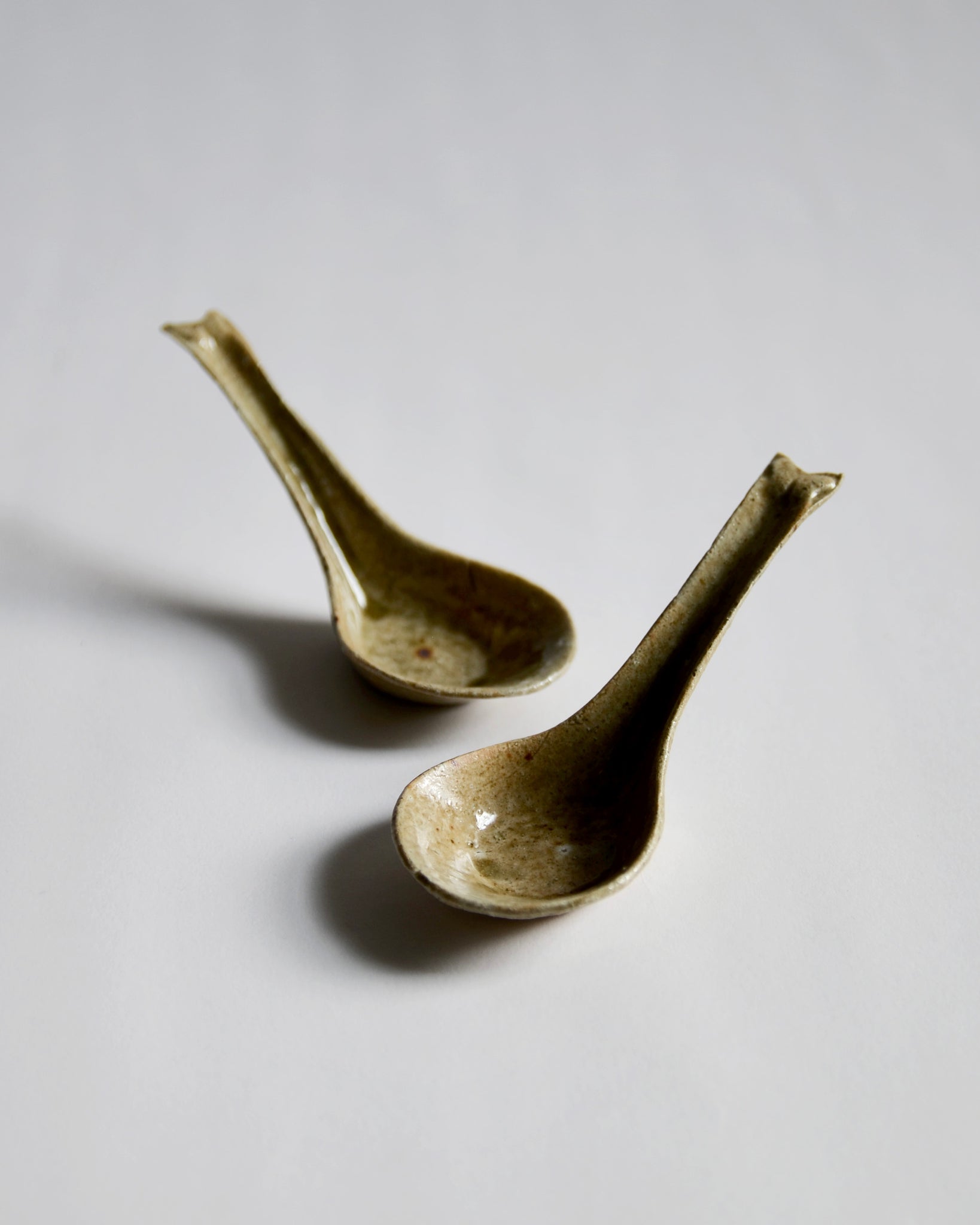 Front view of 2 staggered pine ash Ceramic Soup Spoons by Azmaya against white-gray background.