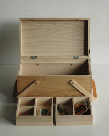 In situation image of open chestnut wood picnic box by Shinsuke Tanabe with the two inner compartments removed and placed in front with sewing materials inside.