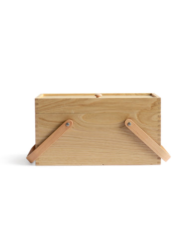 Silhouetted image of chestnut wood picnic box featuring wood joinery on edges with handles down by Shinsuke Tanabe against white background.