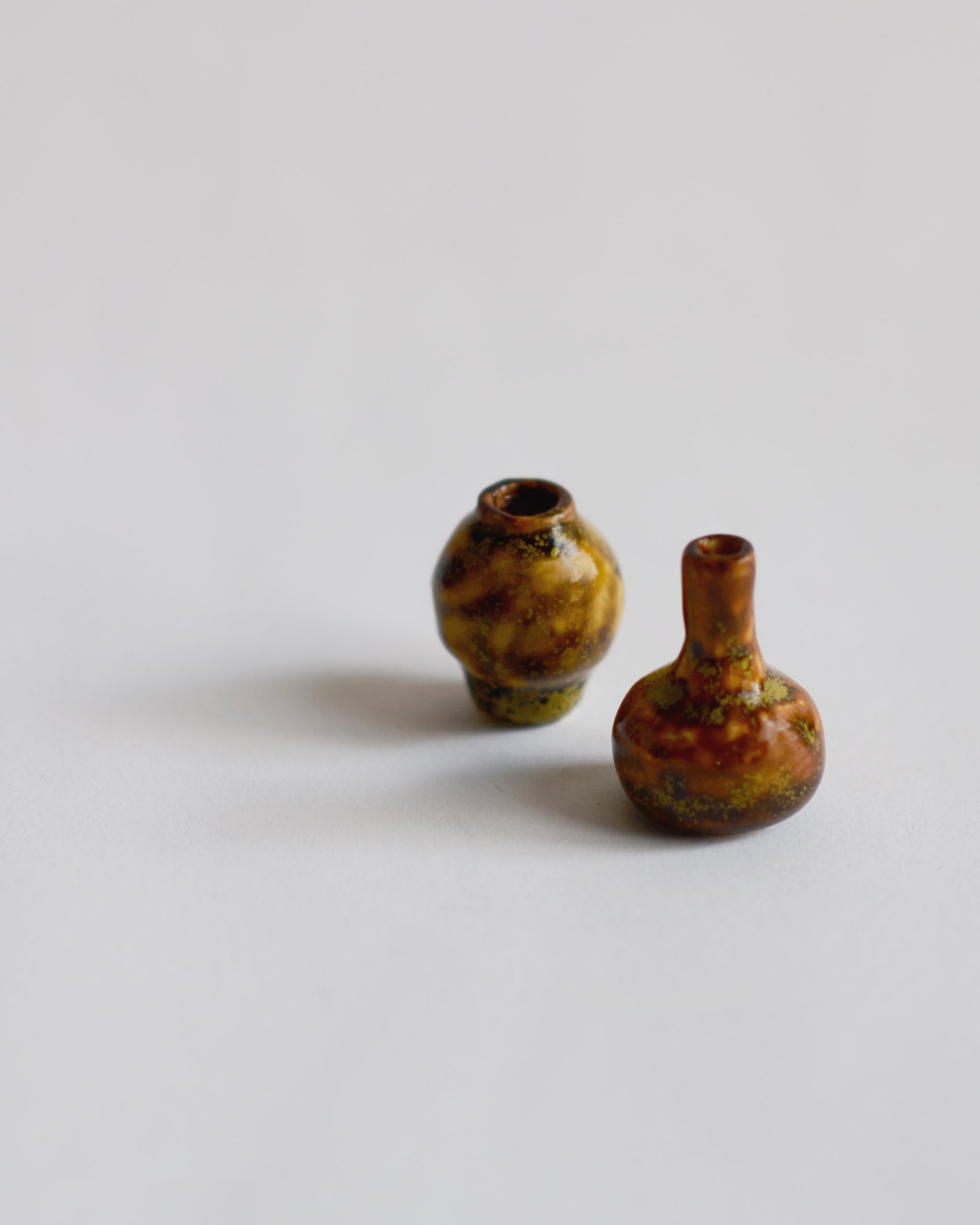  Angled view of 2 brown glazed mini vases from the Mini Vase Set -Duo II by Dani Sujin x Nalata Nalata against white-gray background.