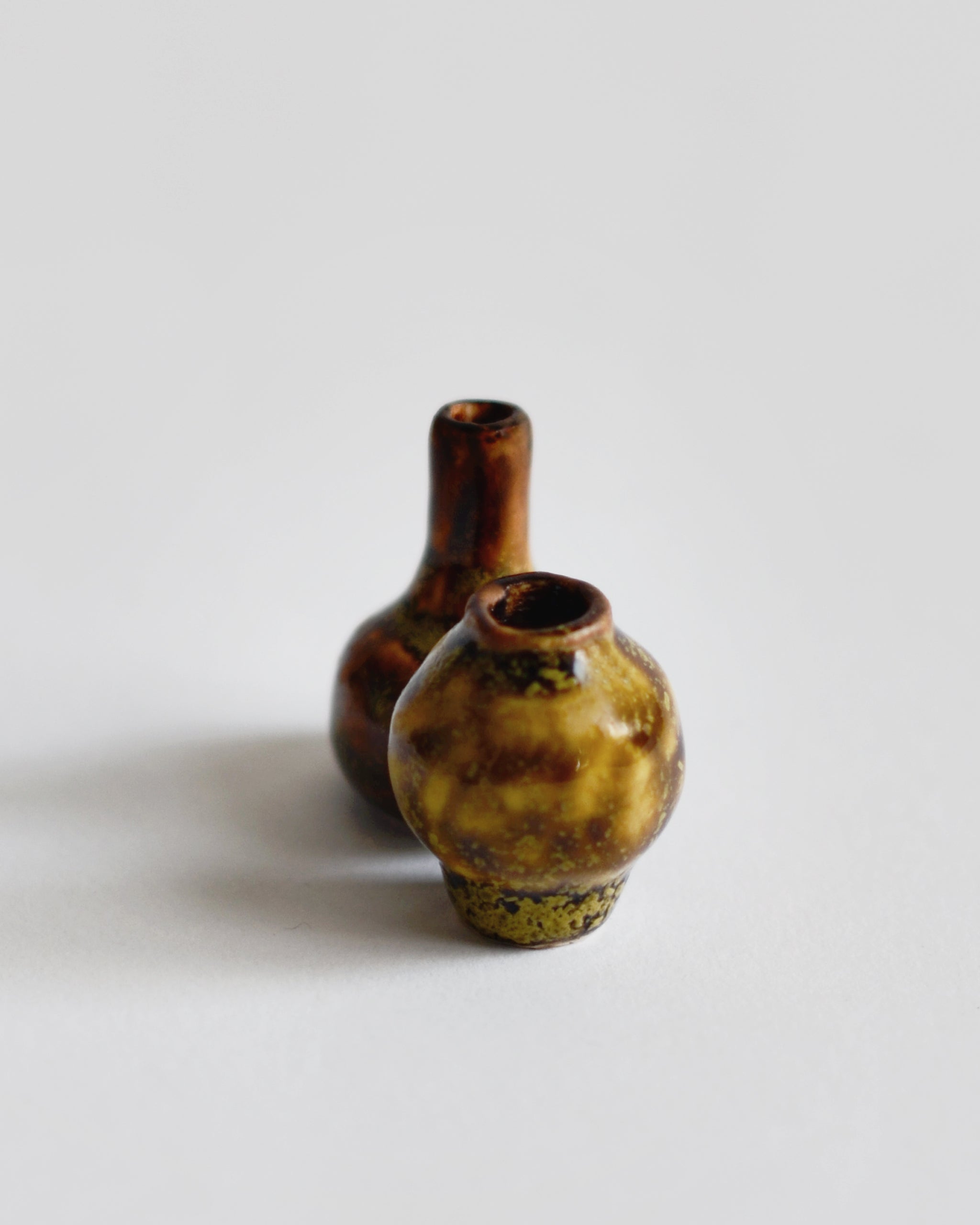 Image of 2 brown glazed mini vases close together from the Mini Vase Set -Duo II by Dani Sujin x Nalata Nalata against white-gray background.