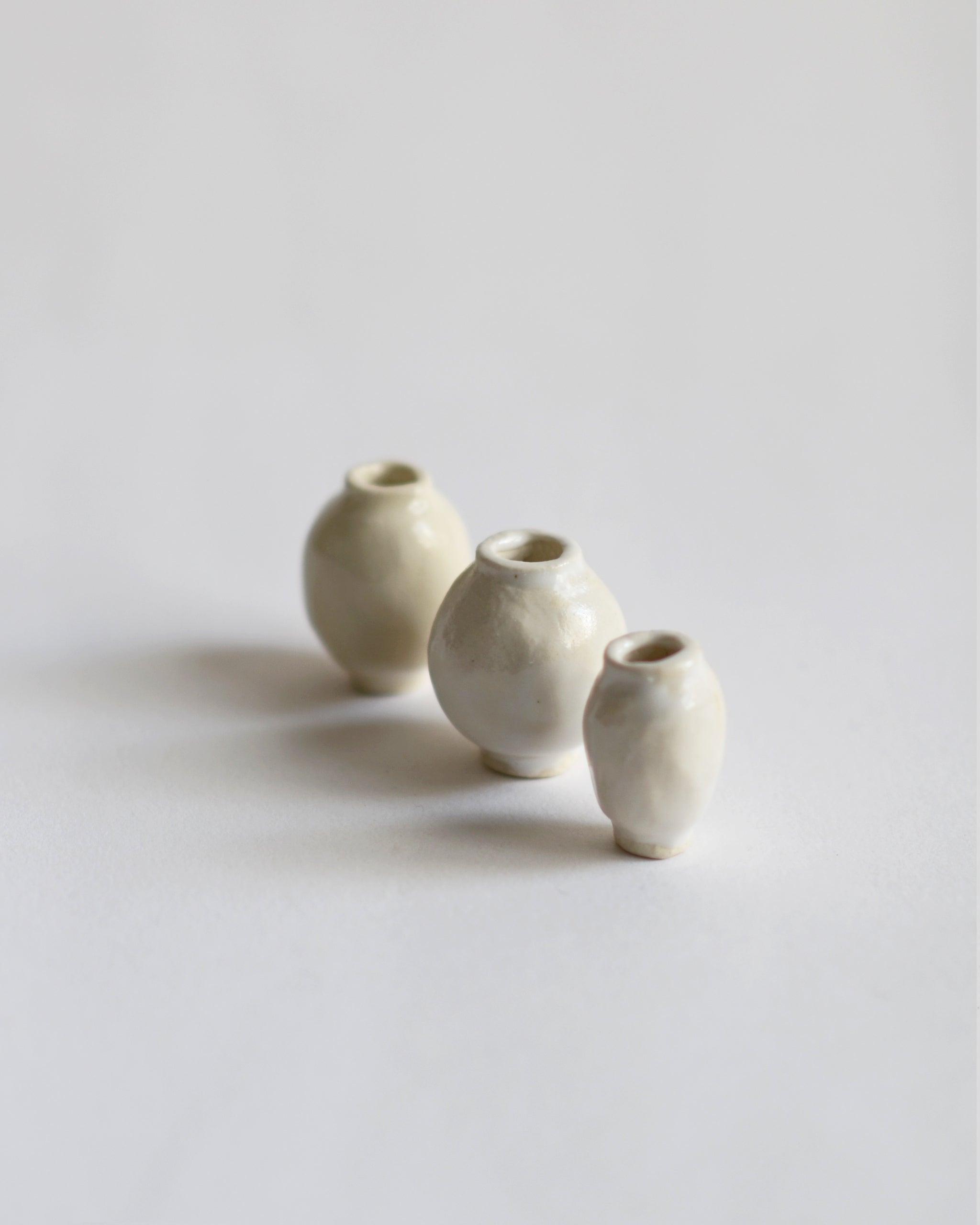 Angled view of 3 varying mini white glazed mini vases from the Mini Vase Set - Trio I by Dani Sujin x Nalata Nalata against white-gray background.