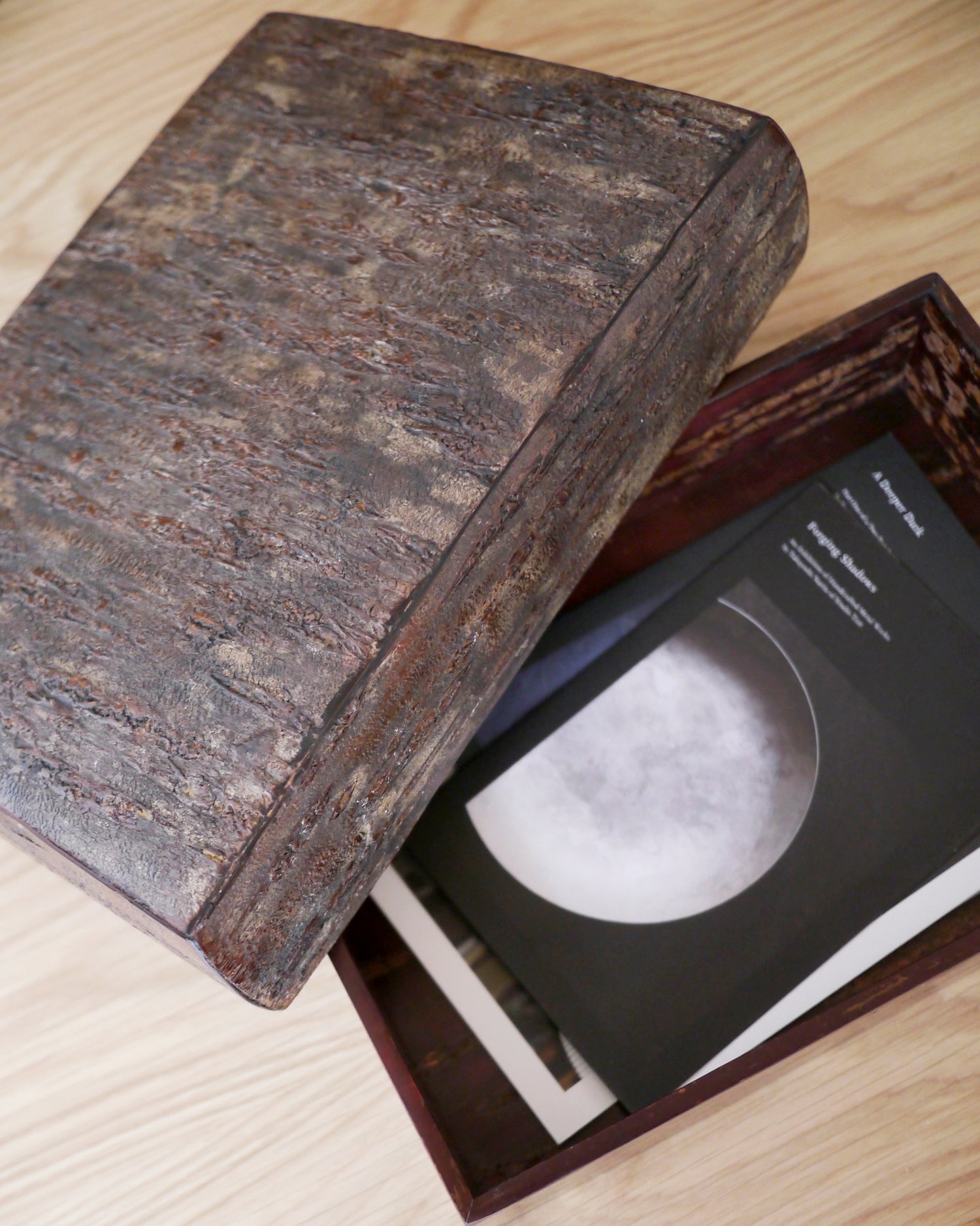 Open wooden box by Denshiro with a pamplets inside with lid laying on side on a light wooden surface