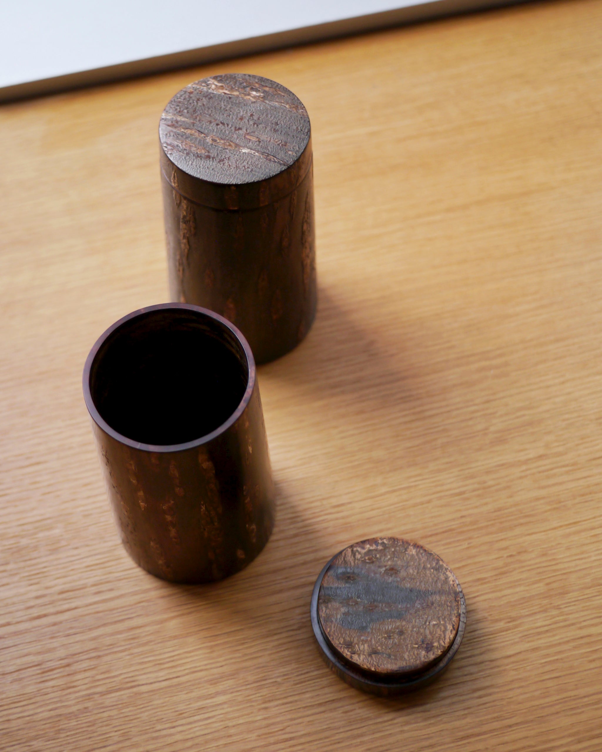 Two wooden cylindrical coffee containers with lids by Denshiro on a wooden surface
