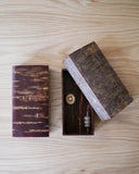 Two wooden boxes by Denshiro - one smooth wood and the other raw cherry bark wood with lid open, showing the interior of tops, all on a wooden surface