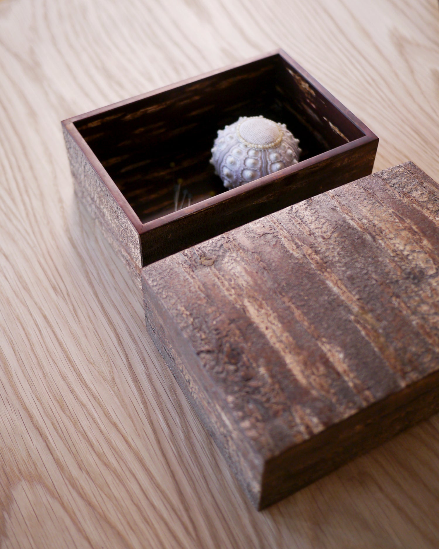 Open wooden box with a textured lid by Denshiro with a sea urchin pin cusion in the interior of the box on a wooden surface