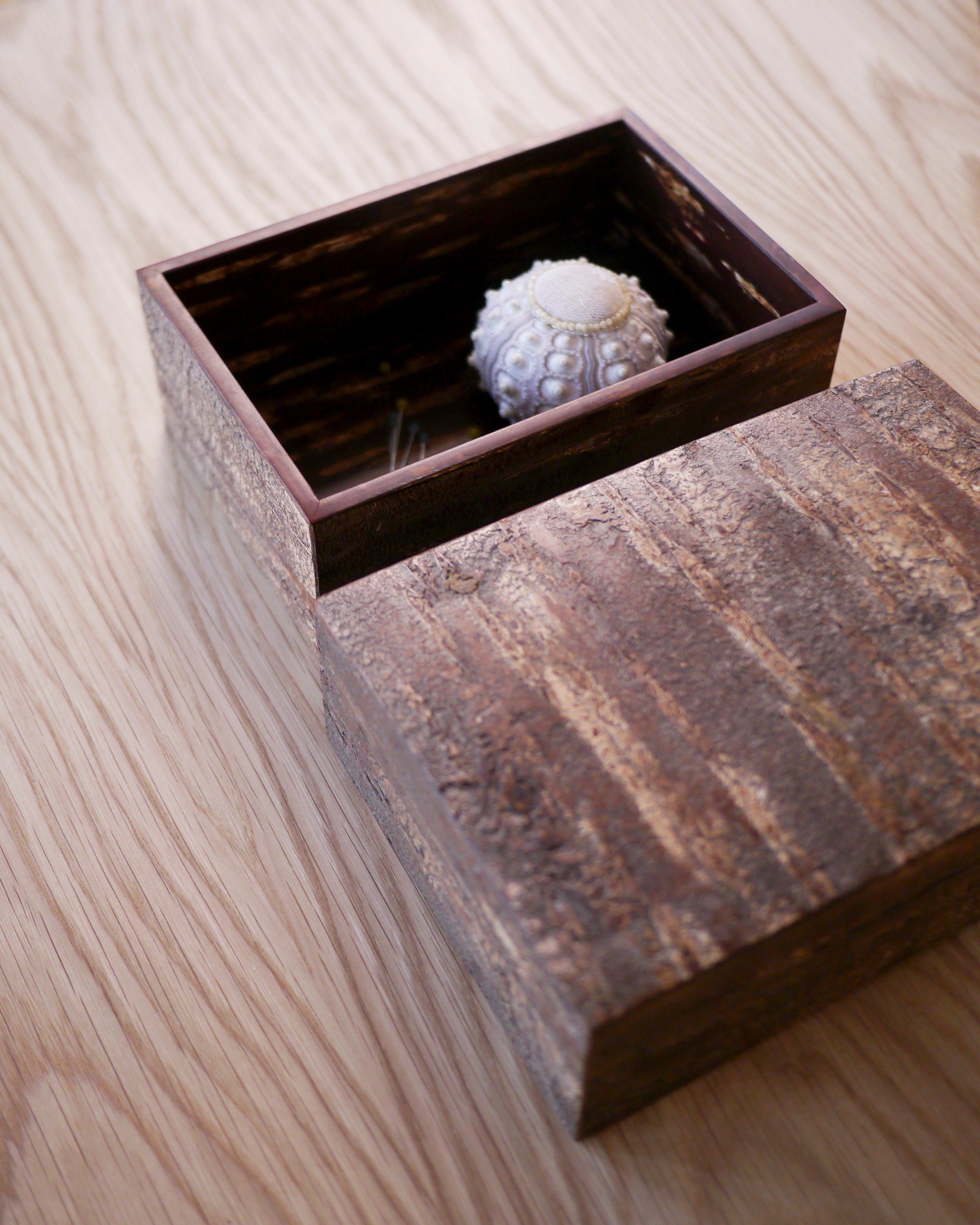 Open wooden box with a textured lid by Denshiro with a sea urchin pin cusion in the interior of the box on a wooden surface