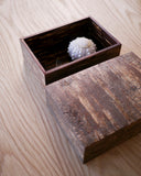 Open wooden box with a textured lid by Denshiro with a sea urchin pin cusion in the interior of the box on a wooden surface