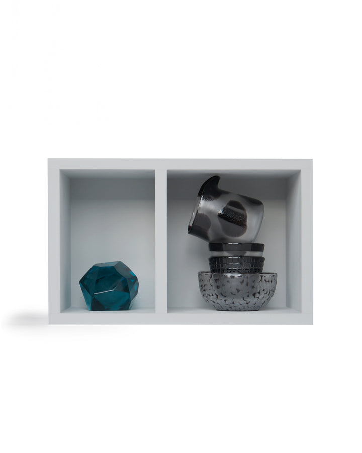 Silhouetted relife composition no.1 by factory zoomer against white background. Light gray wall fixture box is divided into two compartments - jewelry cut paperweight on the left, and a stack of carved bowl, two mini-choko glasses, and cow pitcher on the right.