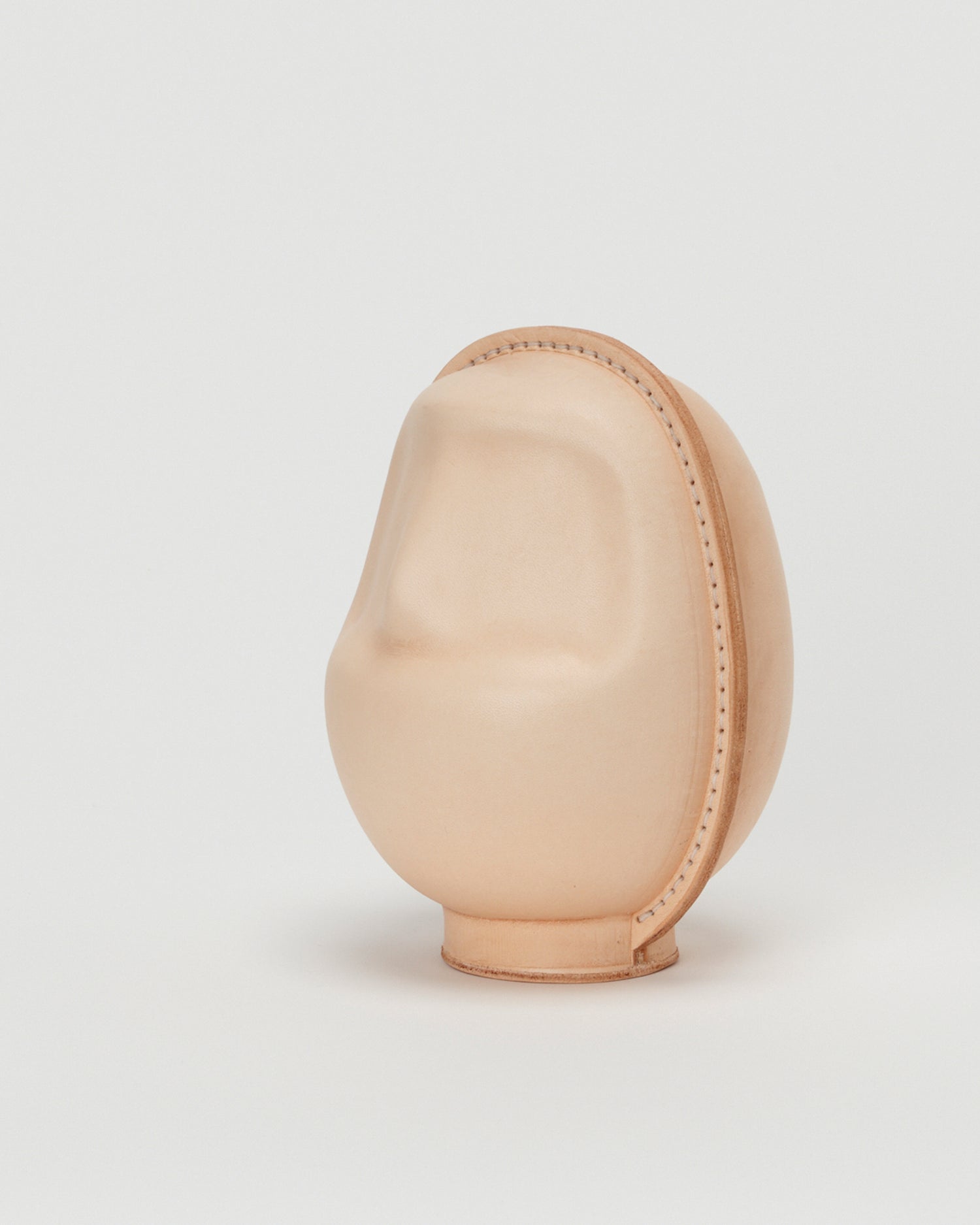 Side view of large leather Daruma doll by Hender Scheme in on  a gray background
