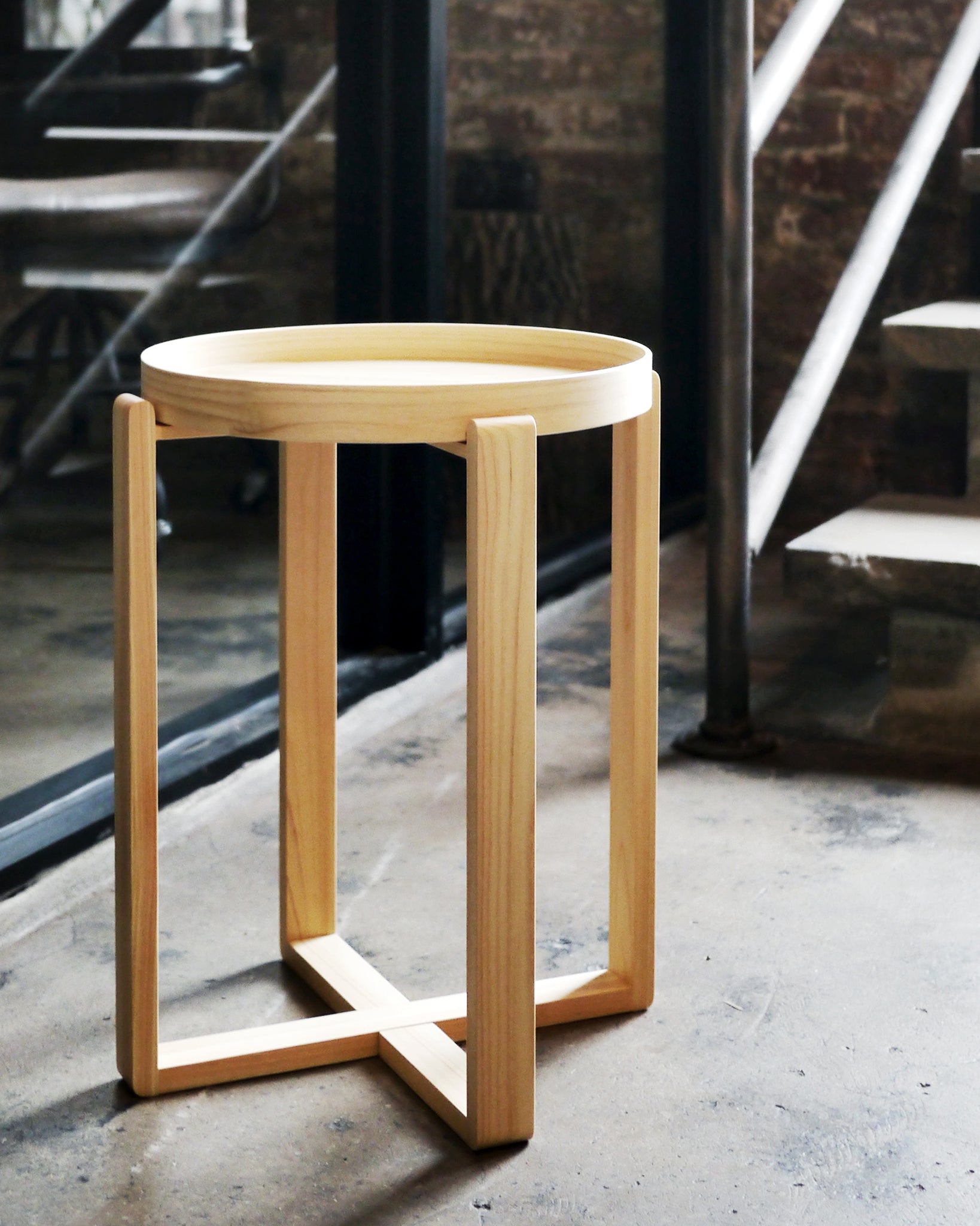 Hinoki magewa tray table placed on a cement floor, with dark brick wall and steel frames and stairs in the background.
