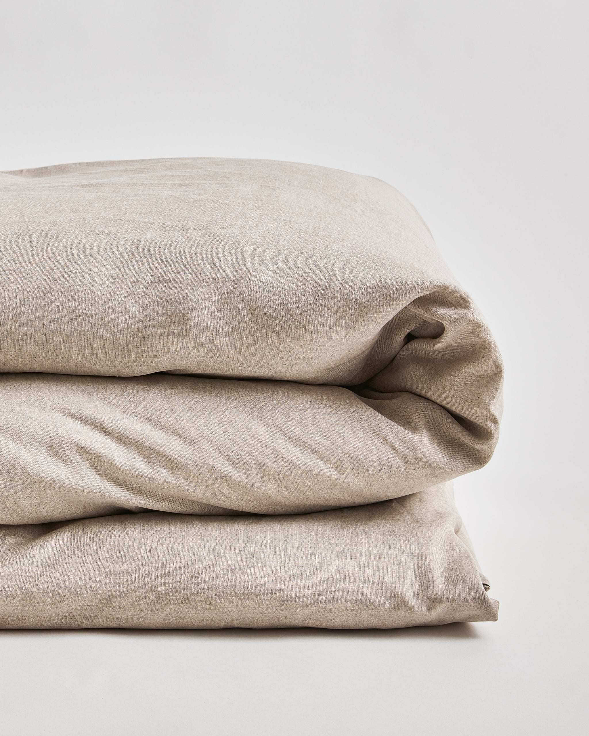 Up-close of unbleached linen duvet cover on a duvet folded on a gray background