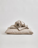 Stack of unbleached linen folded sheets on a pillow by Iwata on a gray 