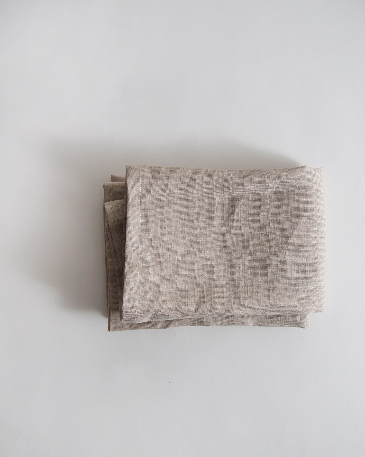 Folded unbleached linen pillow case by Iwata on a gray background