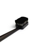 Angled and cropped view of dark long wooden jiva body brush by Shaquda laying against white background. 