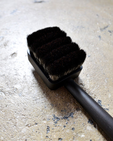 Close-up image of bristles of dark long wooden jiva body brush by Shaquda on rough cement surface. 