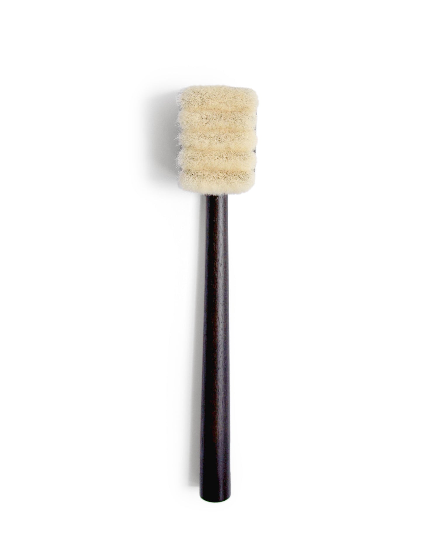 Silhouetted image of long jiva body brush with dark wood handle and light bristles by Shaquda against white background.