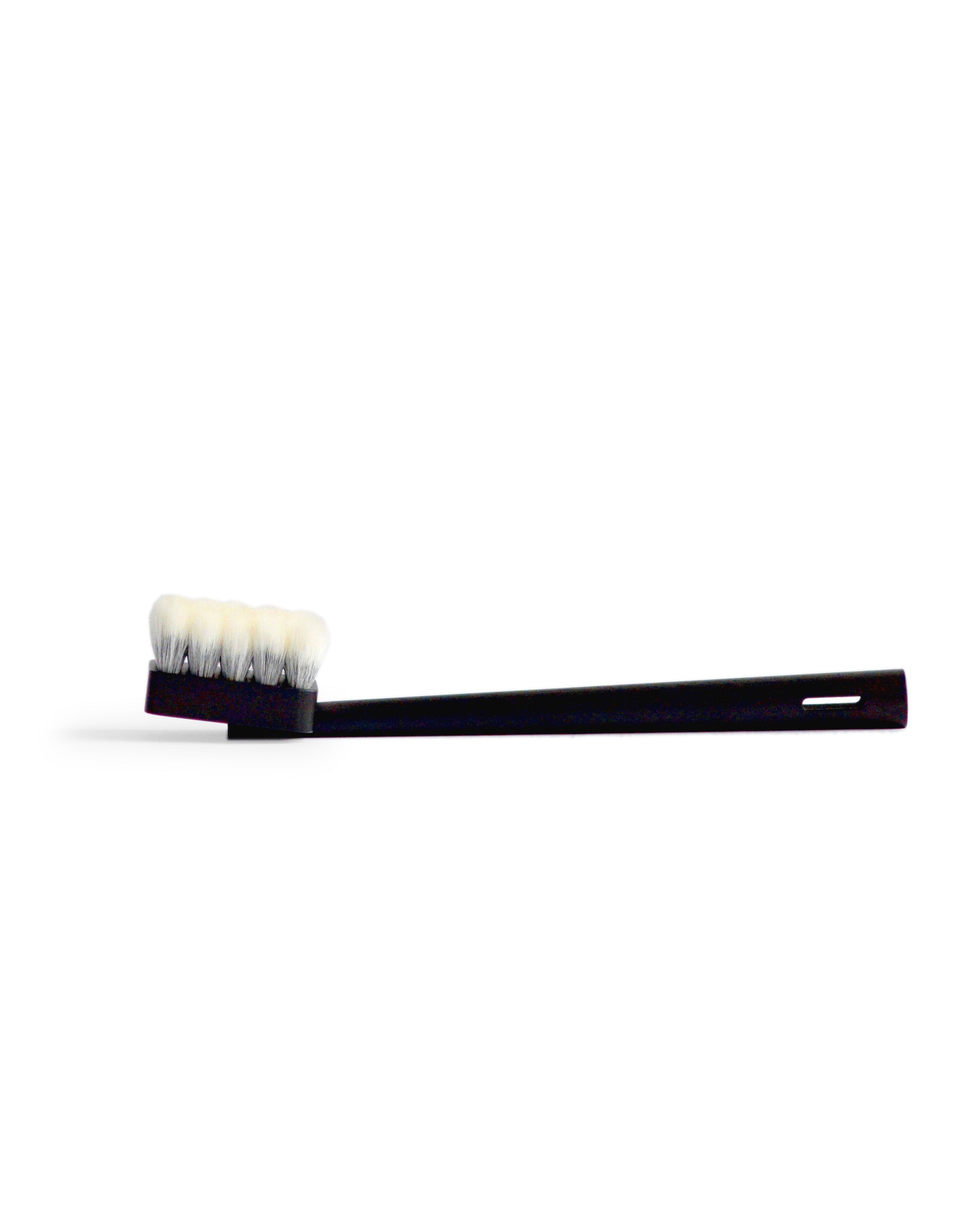 Side view of long jiva body brush with dark wood handle and light bristles by Shaquda laying against white background.