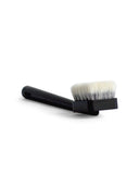 Forshortened image of long jiva body brush with dark wood handle and light bristles by Shaquda laying against white background.