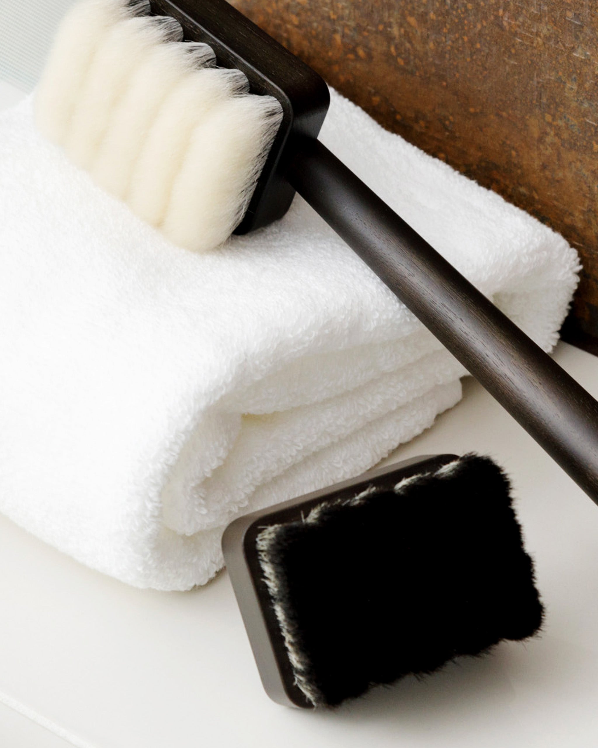In situation image of long jiva body brush with dark wood handle and light bristles by Shaquda and short body brush with dark bristles against white towel.