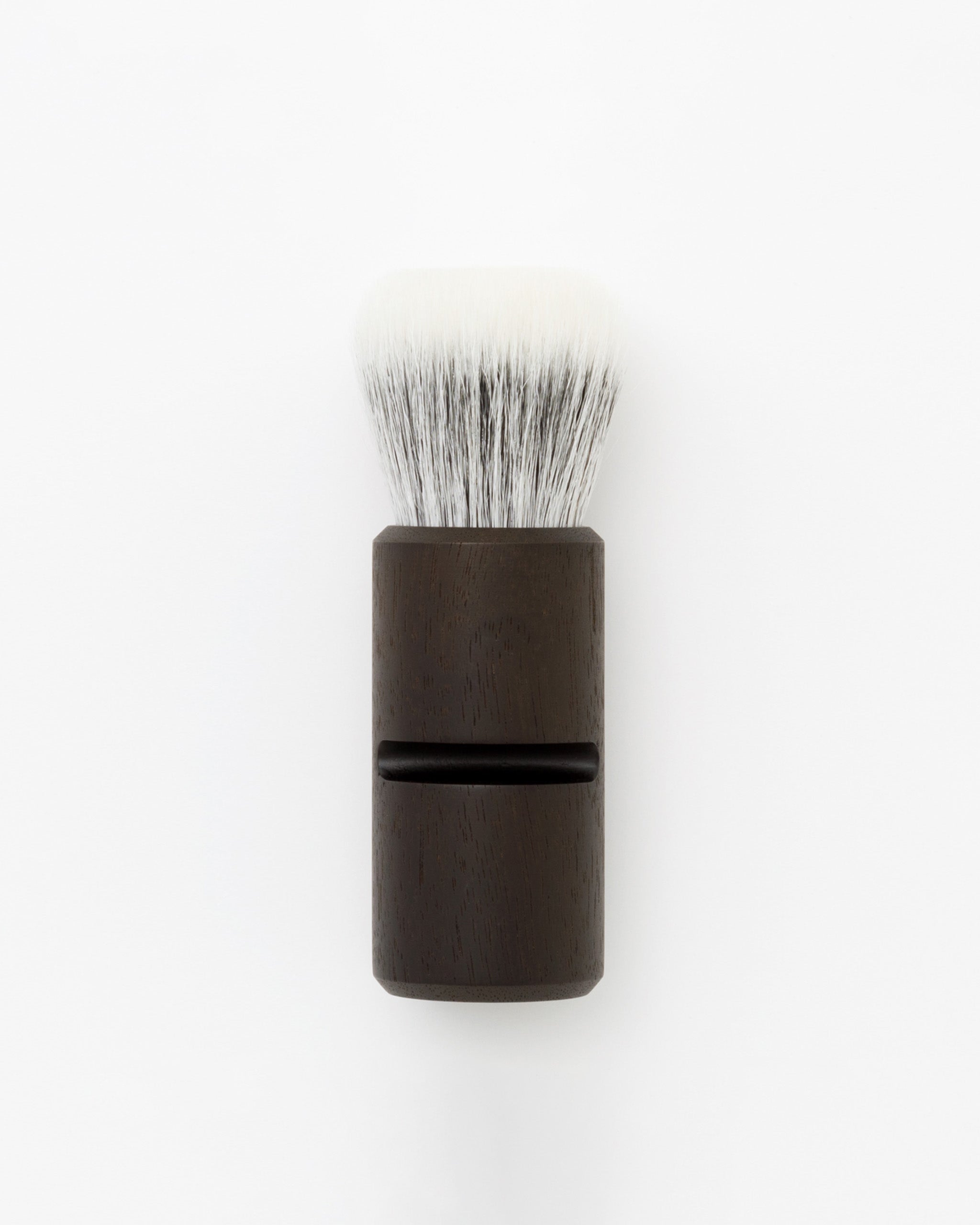  Silhouetted image of soft Jiva face cleansing and shaving series walnut, boar bristle, and goat hair brush by Shaquda against white-gray background.