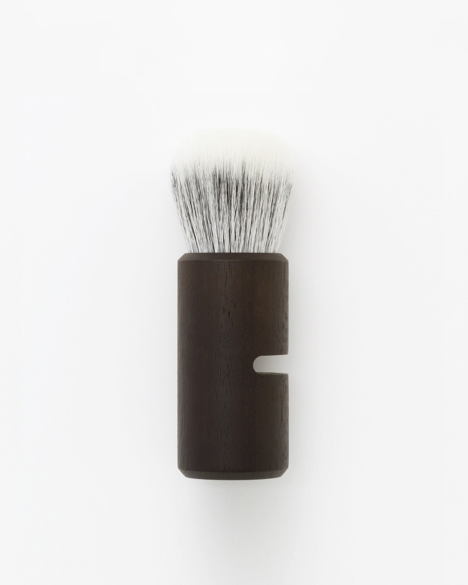 Silhouetted image of soft Jiva face cleansing and shaving series walnut, boar bristle, and goat hair brush by Shaquda against white-gray background.