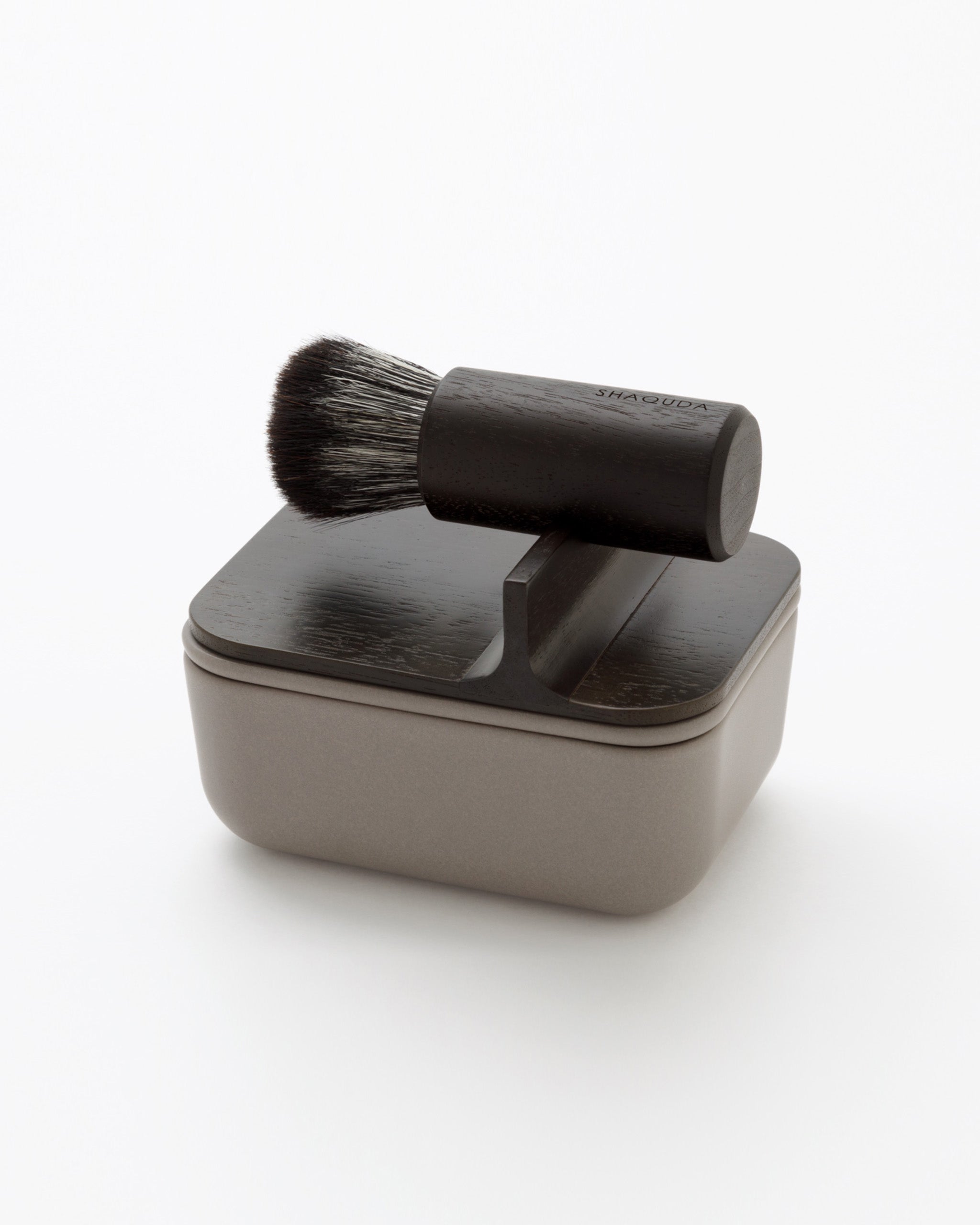 Angled image of hard Jiva face cleansing and shaving series with porcelain bowl and walnut, boar bristle, and goat hair brush by Shaquda against white-gray background. 