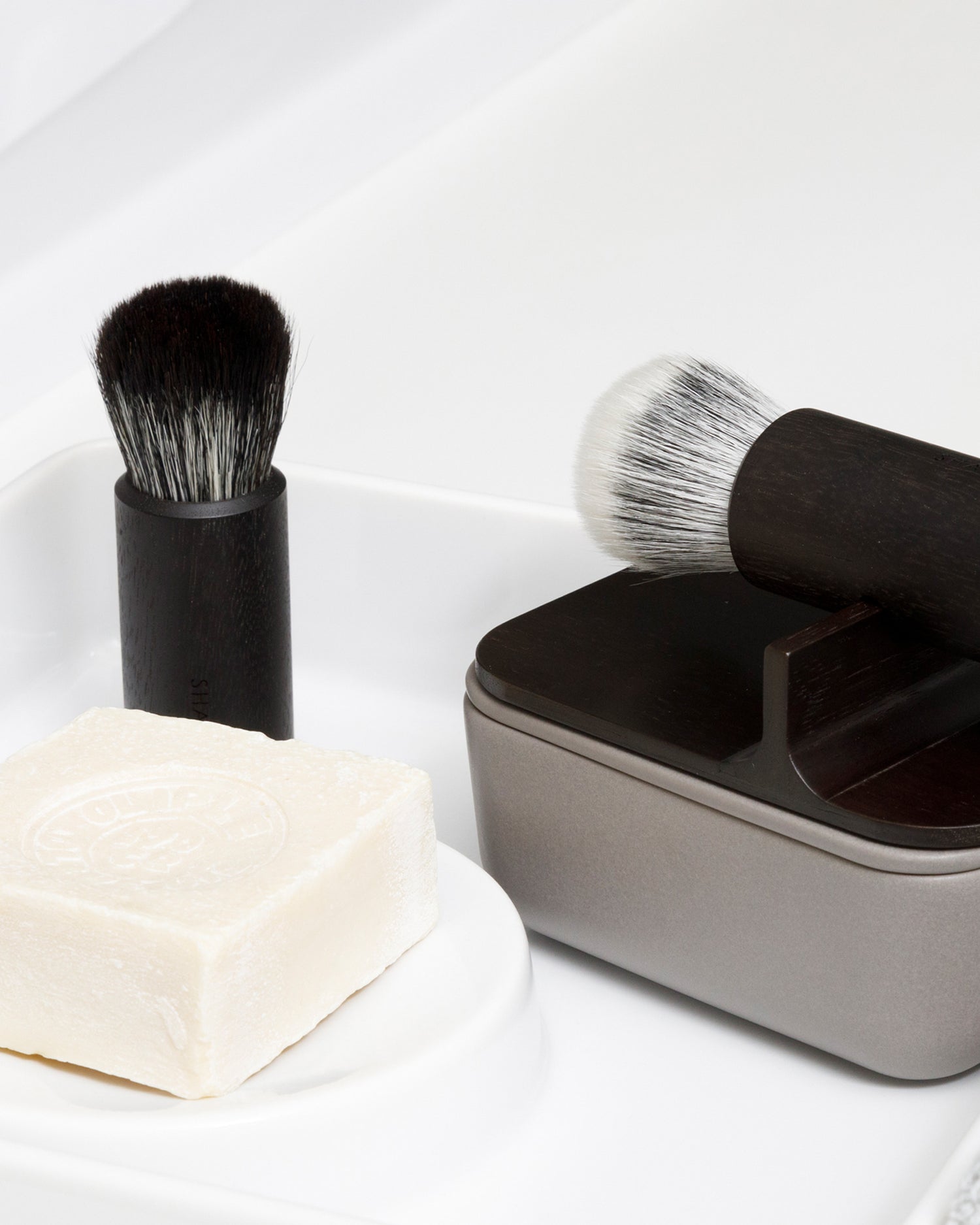 In situation image of hard Jiva face cleansing and shaving series next to bar of soap and additional shaving brush on ceramic tray.