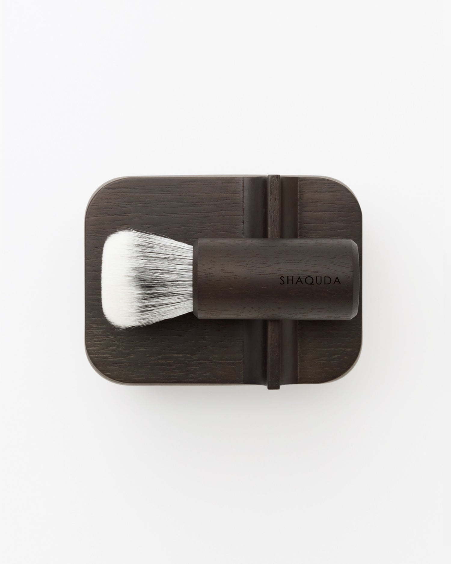 Bird's-eye-view of soft Jiva face cleansing and shaving series with walnut, boar bristle, and goat hair brush on top of porcelain bowl by Shaquda against white-gray background.