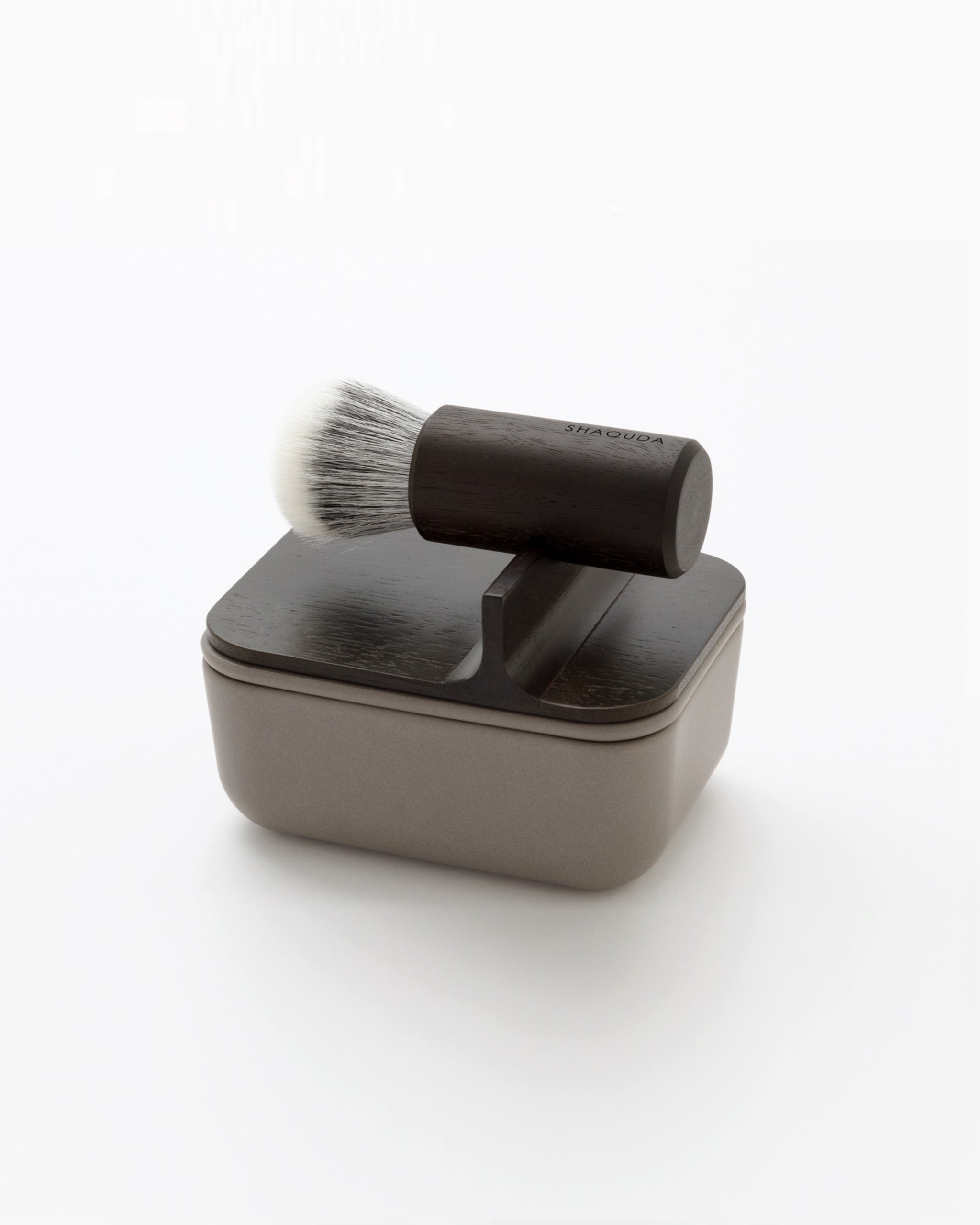 Angled image of soft Jiva face cleansing and shaving series with porcelain bowl and walnut, boar bristle, and goat hair brush by Shaquda against white-gray background.