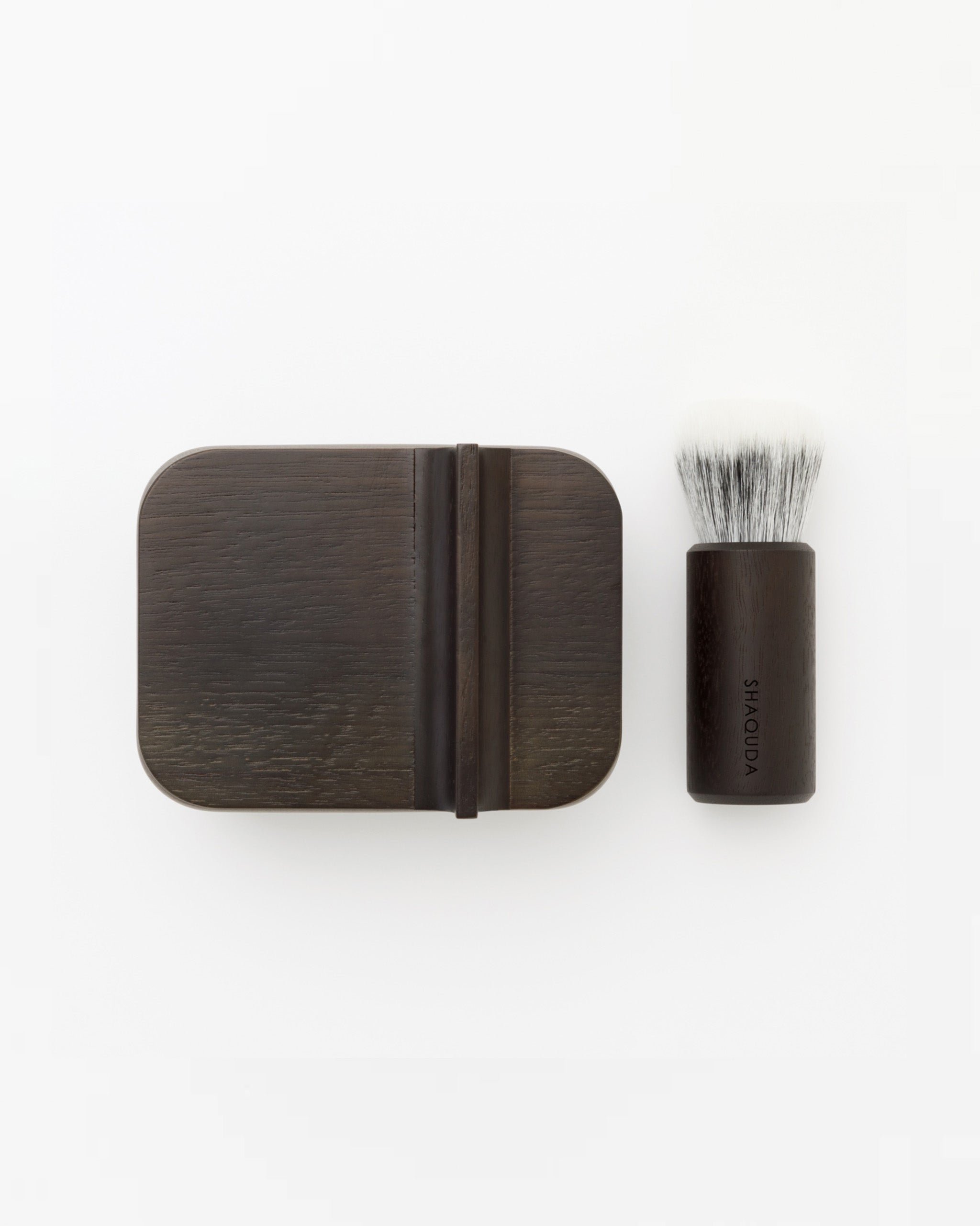 Image of soft Jiva face cleansing and shaving series with porcelain bowl next to walnut, boar bristle, and goat hair brush by Shaquda against white-gray background.