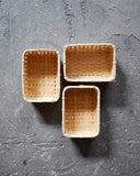 In situation image of three small woven rectangular baskets by Kochosai Kosuga on dark cement surface.